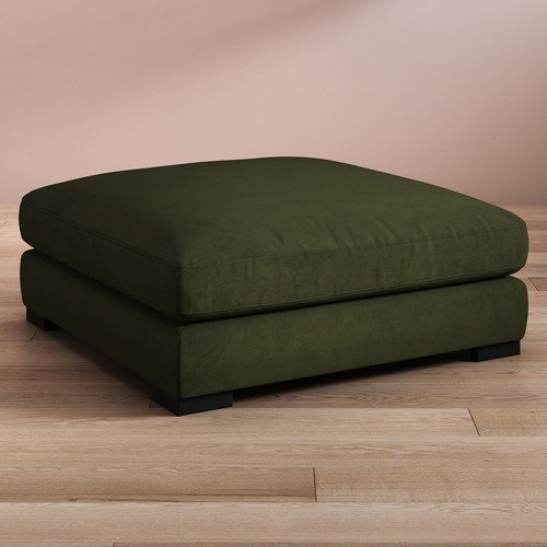 Rectangular green velvet ottoman with cushioned top and short black legs on a wooden floor.