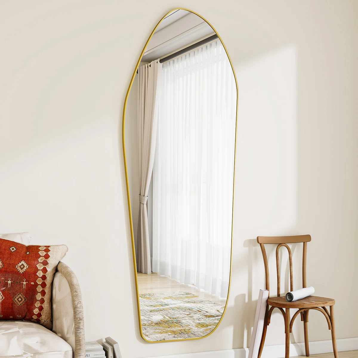 Arched gold-framed mirror reflecting a modern bathroom with white freestanding tub, brushed gold faucet, pendant light, arched windows, and a woven basket on wooden flooring.
