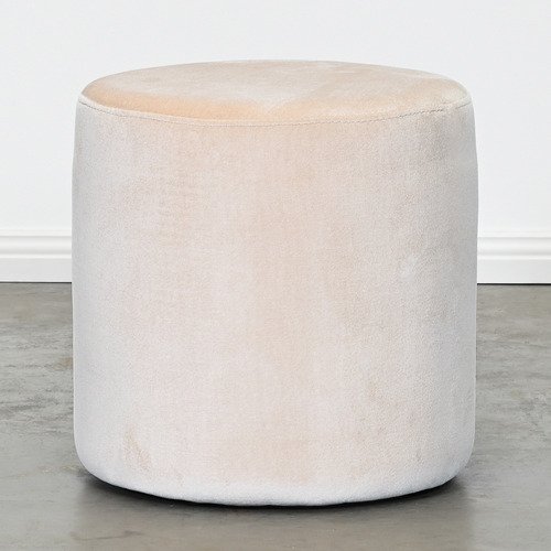 Round light beige velvet ottoman with smooth upholstery and no visible base, placed on a concrete floor against a white wall.