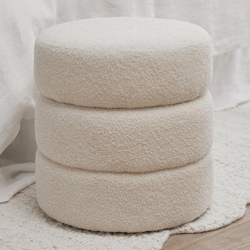 Three stacked round ottomans in light beige recycled teddy fabric on a soft rug in a cozy room.