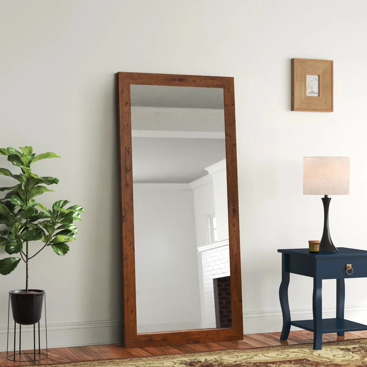 Rectangular full-length mirror with a natural wood frame leaning against a wall in a bright interior room.