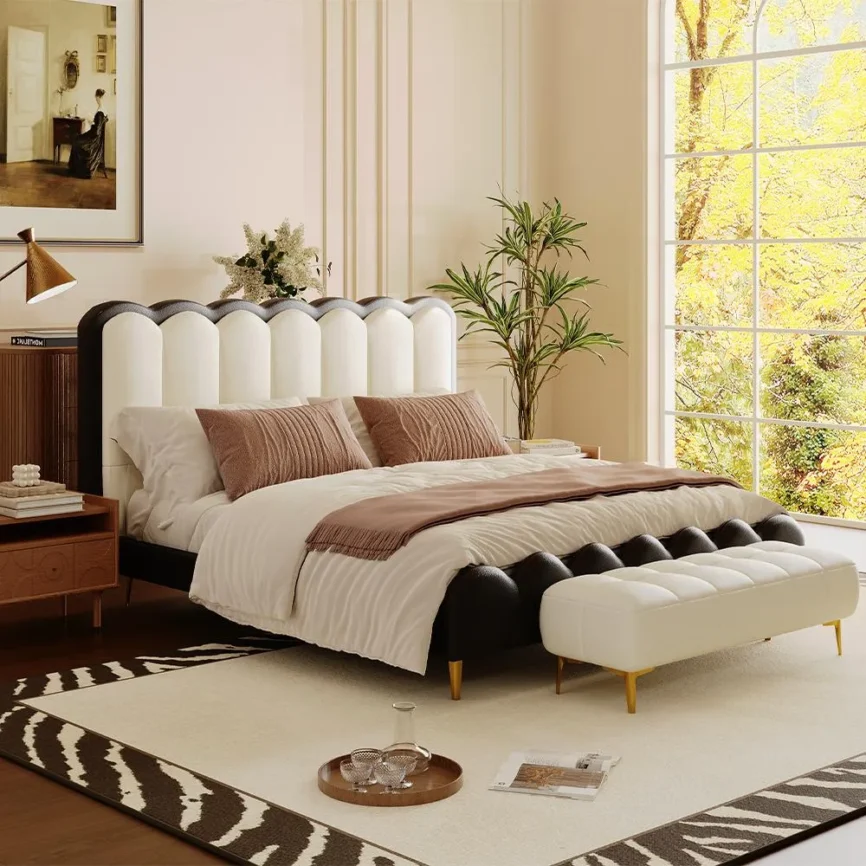 A luxurious bedroom featuring a scalloped headboard upholstered in alternating black and white segments, paired with a matching bench in white fabric and gold legs.