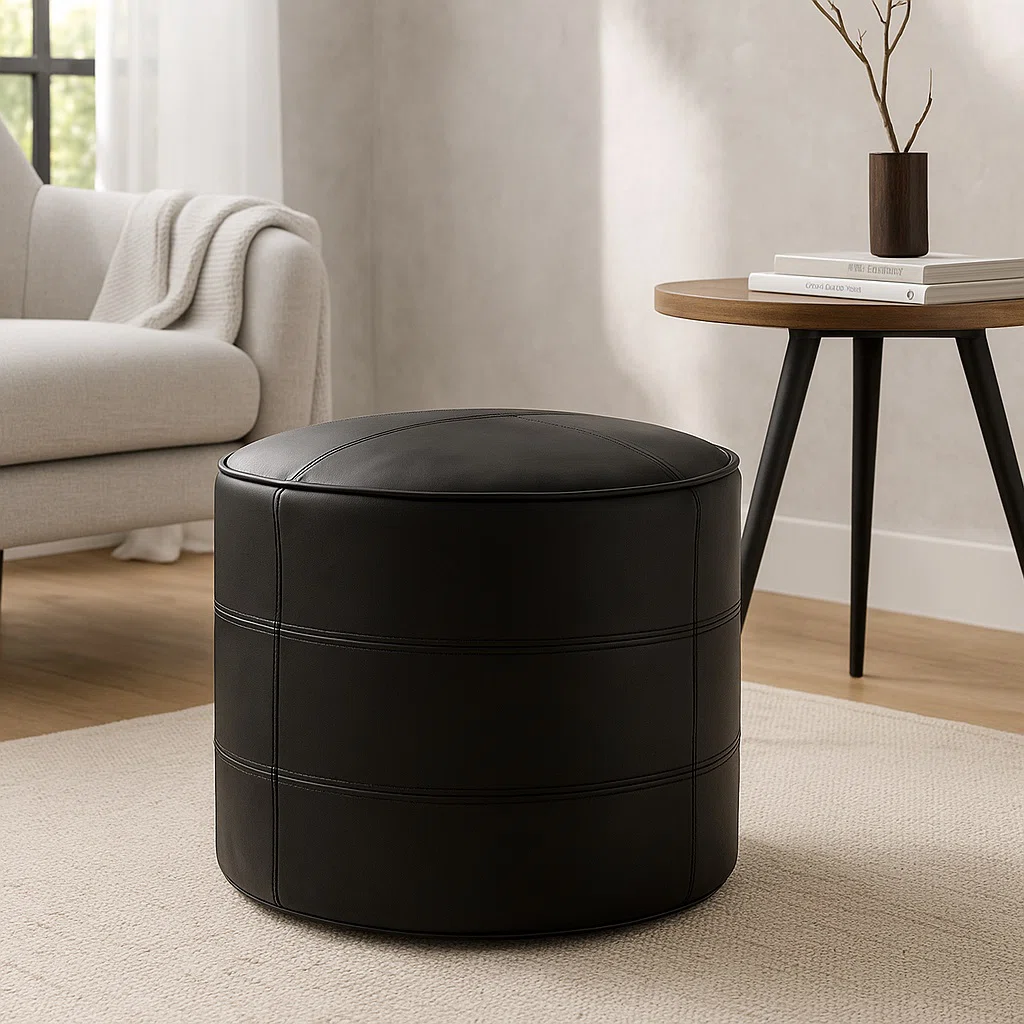 Black leather round pouf with horizontal stitching on a light rug in a modern living room