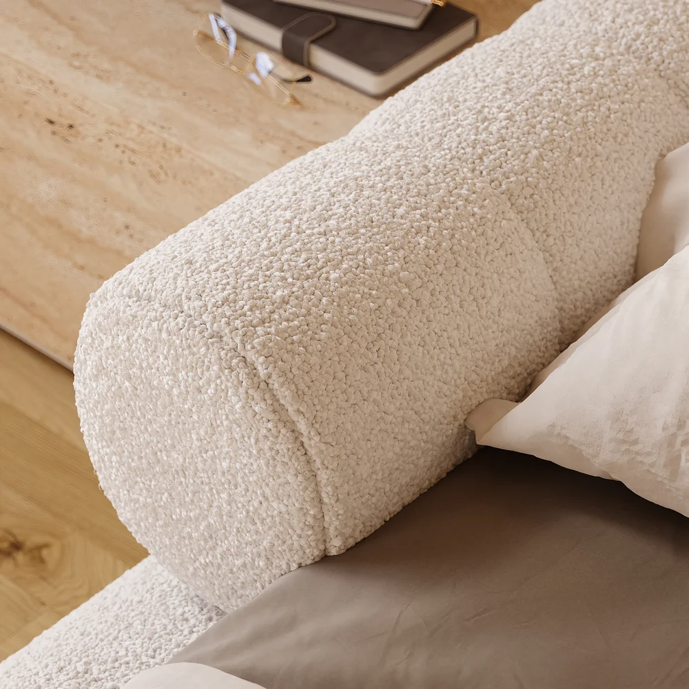 A plush queen-size floor bed upholstered in textured white boucle fabric, featuring a rounded frame and a sculptural headboard