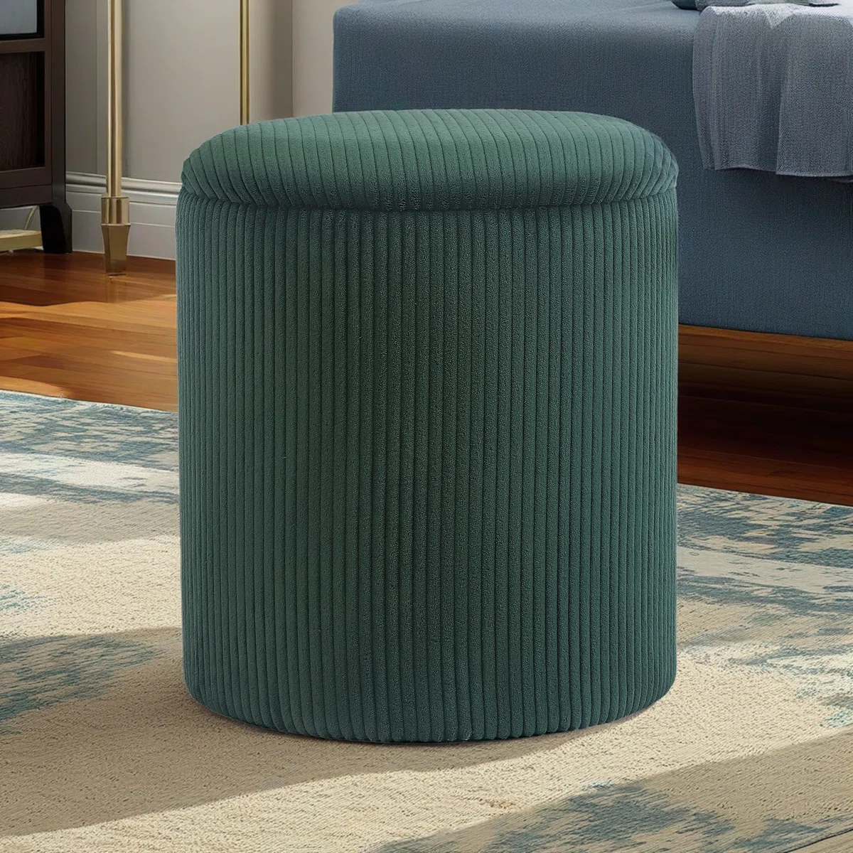 Round green velvet ottoman with vertical ribbing, placed on a patterned rug in a modern room.