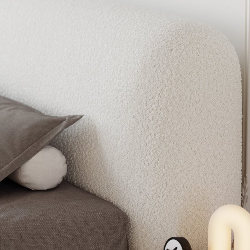 White boucle upholstered bed with padded headboard, gray bedding, and white nightstands in a minimalist bedroom.