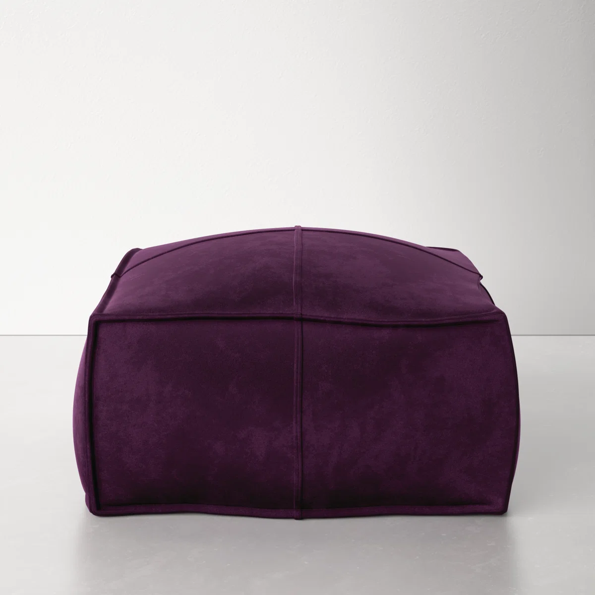 Purple velvet square pouf with panel seams on light floor against white wall