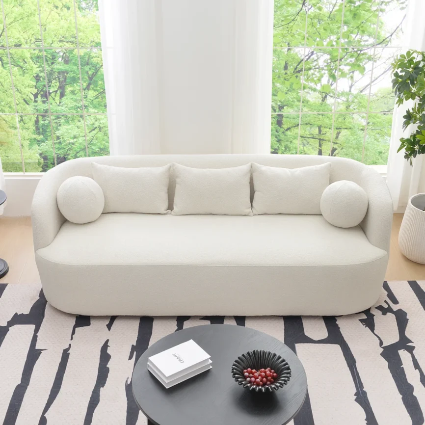 A light beige upholstered sofa with a rounded back and arms, styled in a minimalist living room.