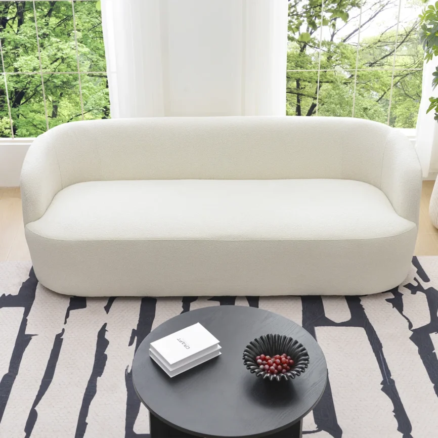 A light beige upholstered sofa with a rounded back and arms, styled in a minimalist living room.