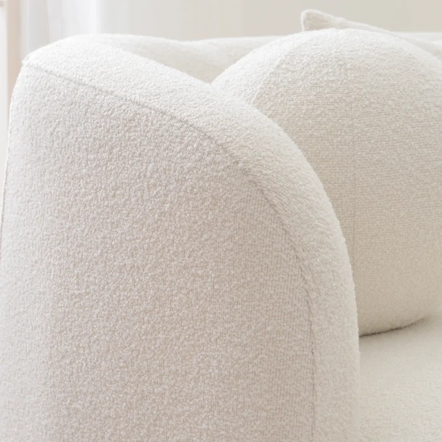 A light beige upholstered sofa with a rounded back and arms, styled in a minimalist living room.