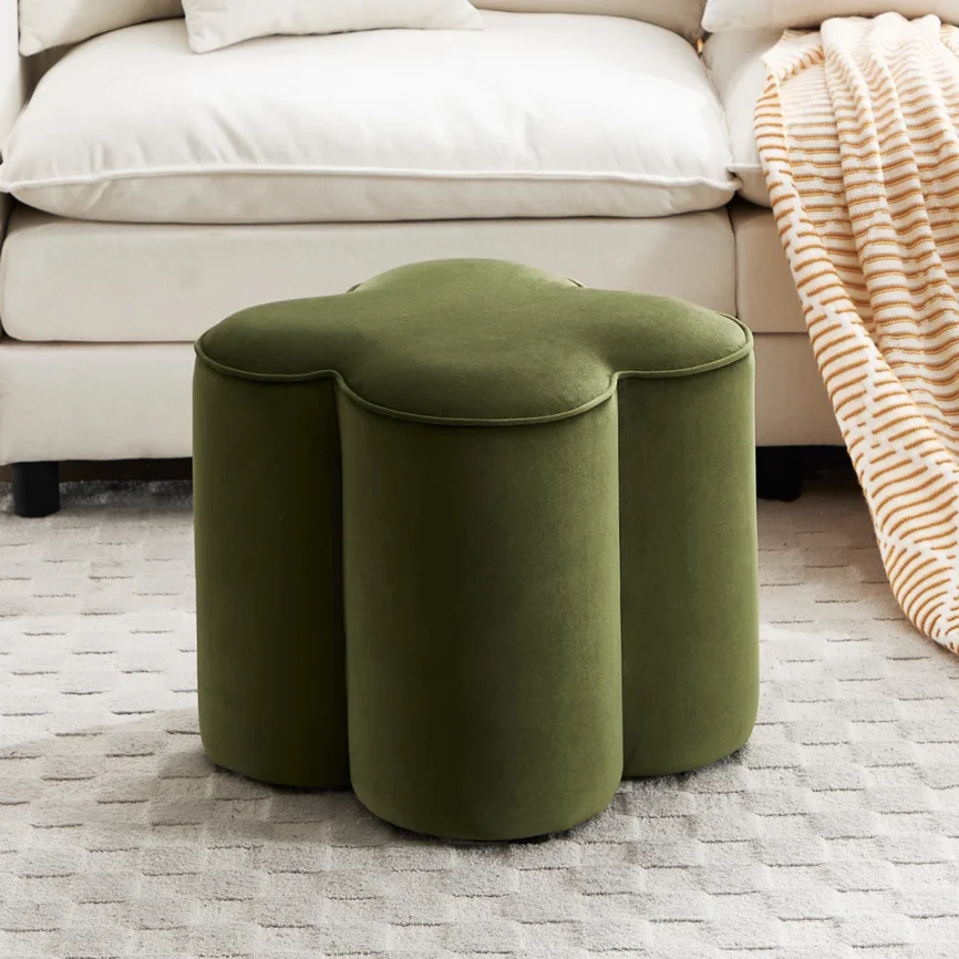 Green petal-shaped upholstered ottoman on a textured rug in a cozy living room setting
