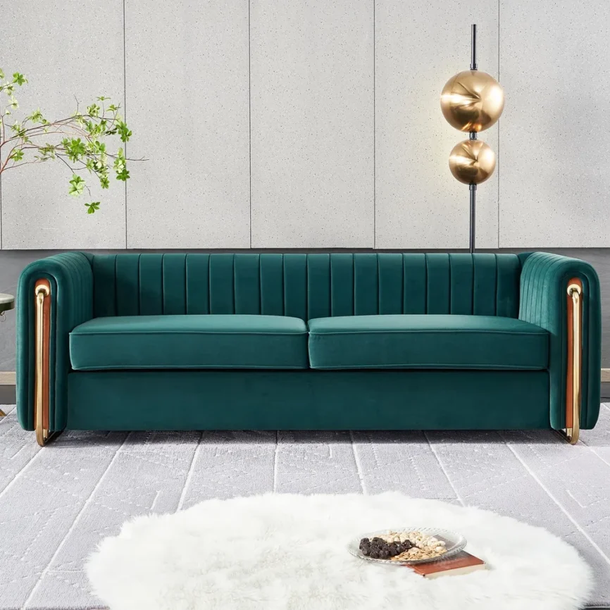 A luxurious green velvet sofa with vertical channel tufting and gold metal accents on the armrests sits atop a textured gray rug
