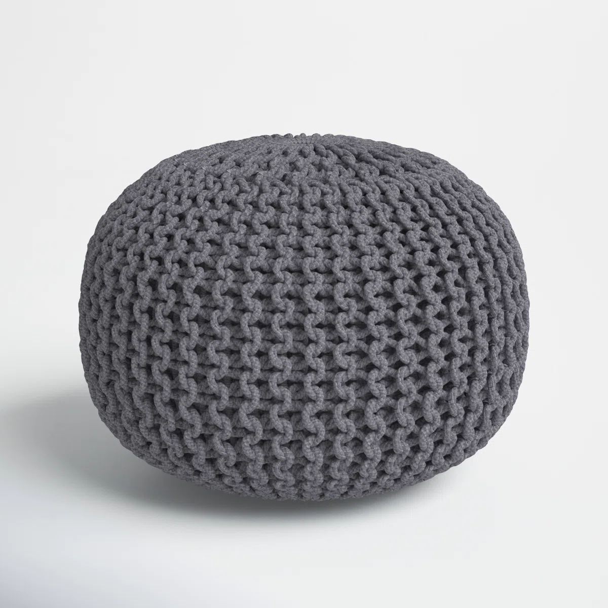 Round knitted pouf ottoman in dark gray yarn with a chunky textured weave, placed on a light floor.