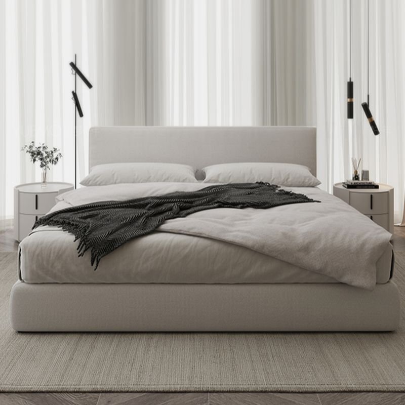 White upholstered panel bed with neutral bedding, round nightstands, and pendant lights in a modern bedroom.
