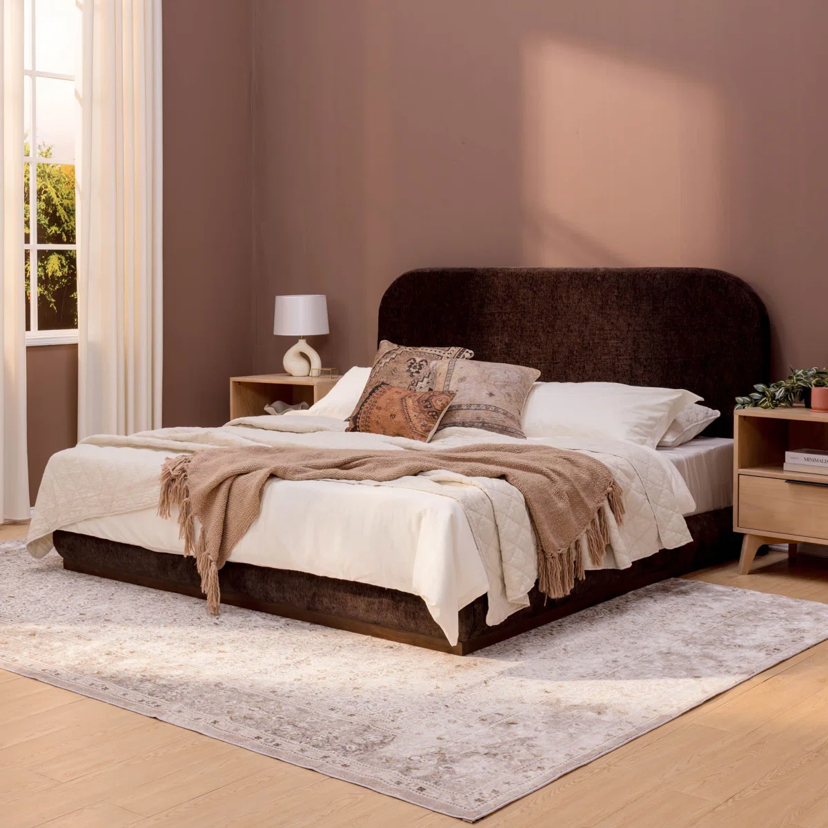 A king-size bed with a dark upholstered headboard, styled in crisp white bedding and layered pillows in neutral tones.