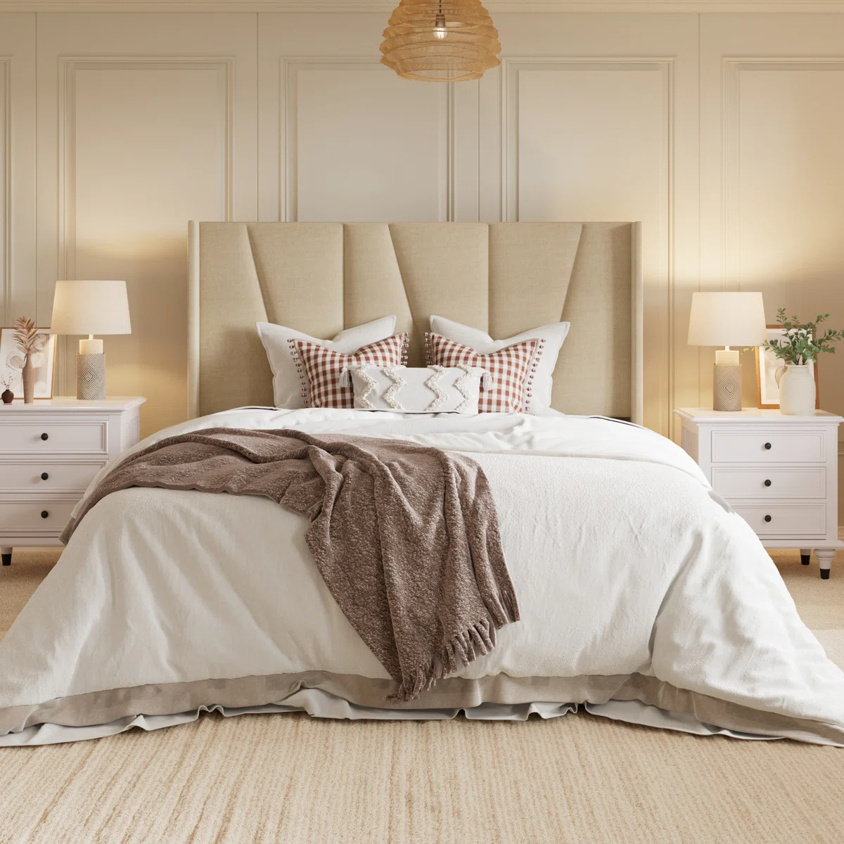 Beige upholstered bed with layered pillows, brown throw, white nightstands, and matching lamps in a cozy bedroom.