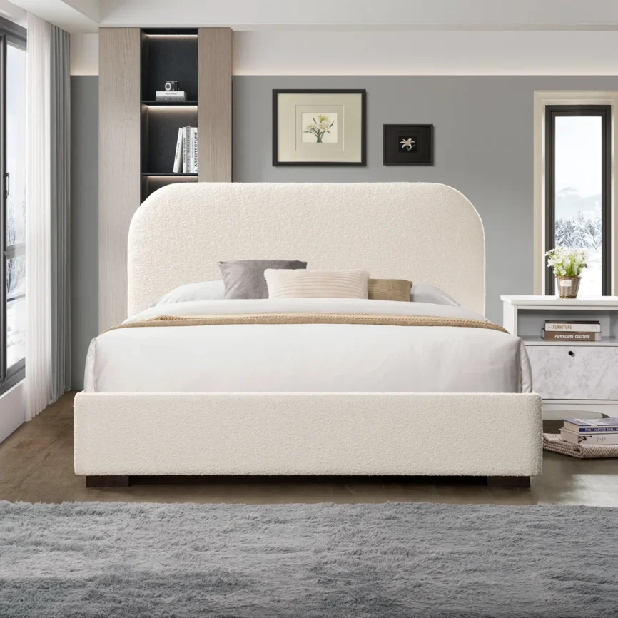Cream boucle bed with rounded headboard, white bedding, neutral pillows, and built-in shelf in a cozy bedroom.