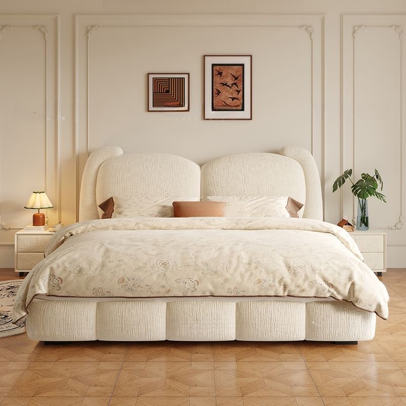 Modern bedroom with upholstered bed, cream floral bedding, nightstands, and warm neutral decor.