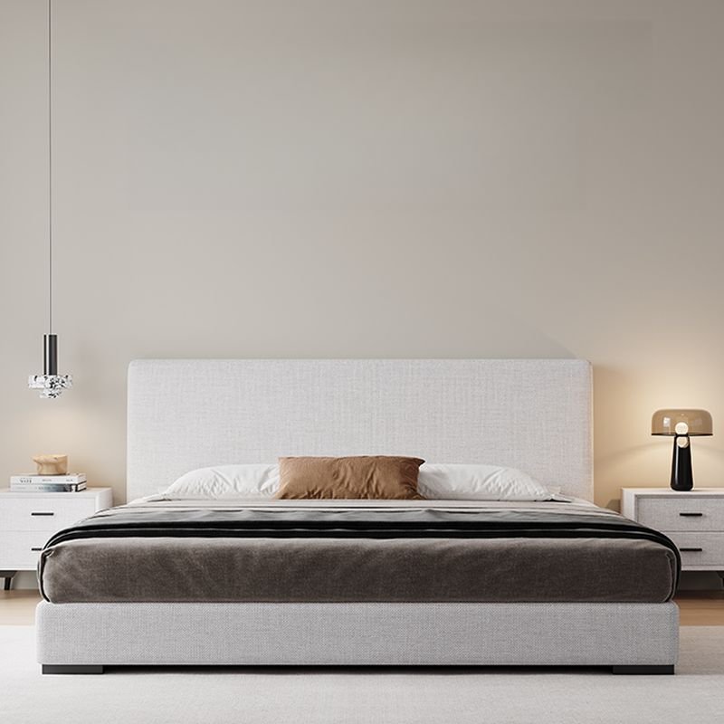 Modern bedroom with light gray upholstered bed, white pillows, pendant light, and neutral decor.