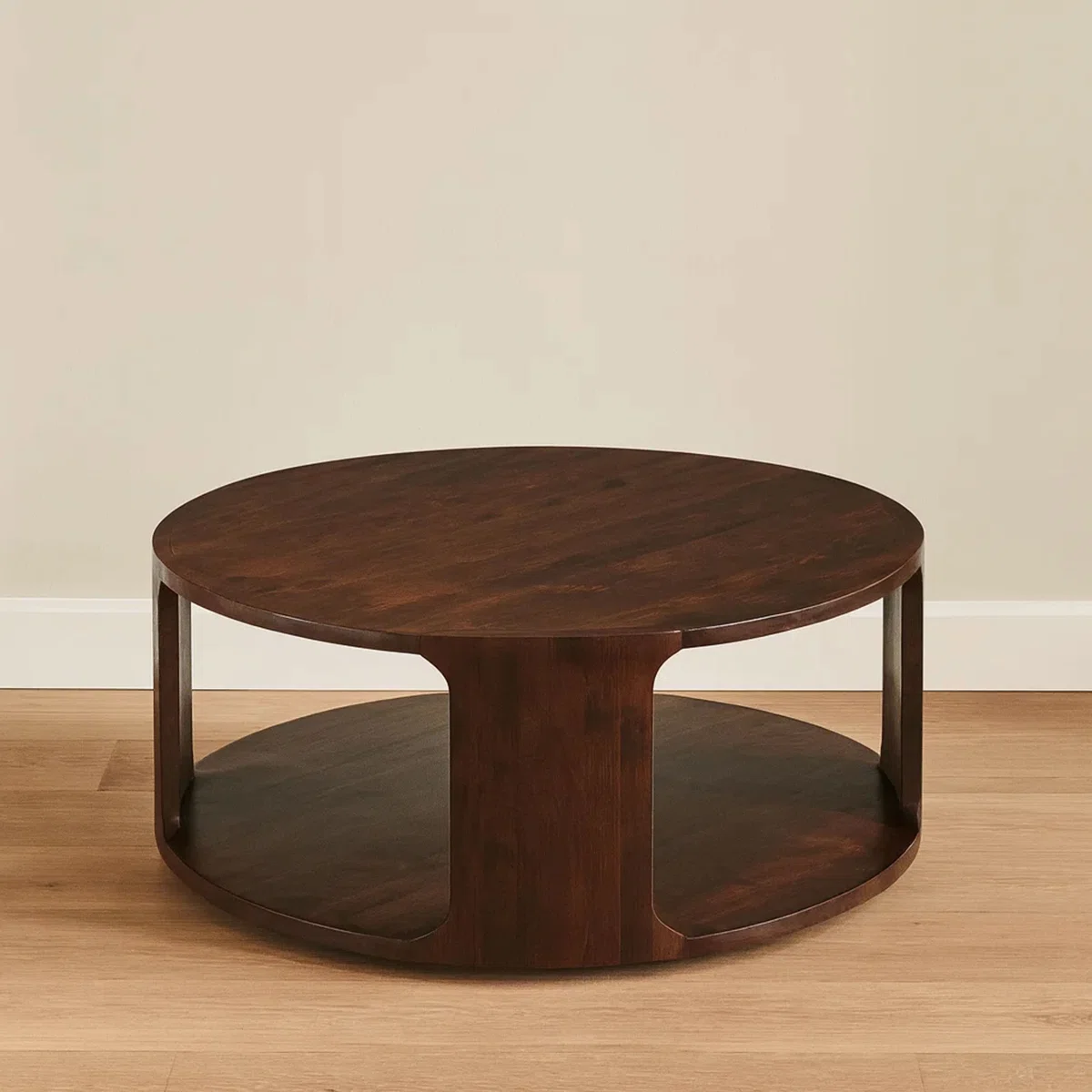 Lyric Round Coffee Table in walnut brown mango wood, 96.5 cm round top with sculptural frame and open lower shelf.